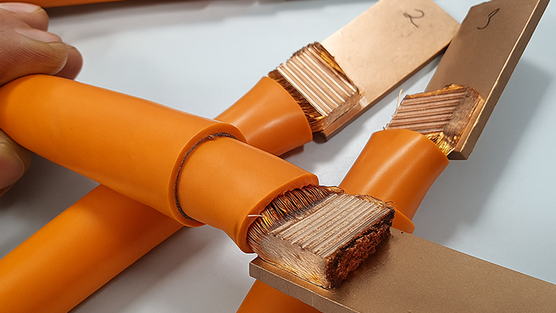 Cables de cobre con aislamiento naranja y extremos de hilos pelados conectados a barras planas de cobre.